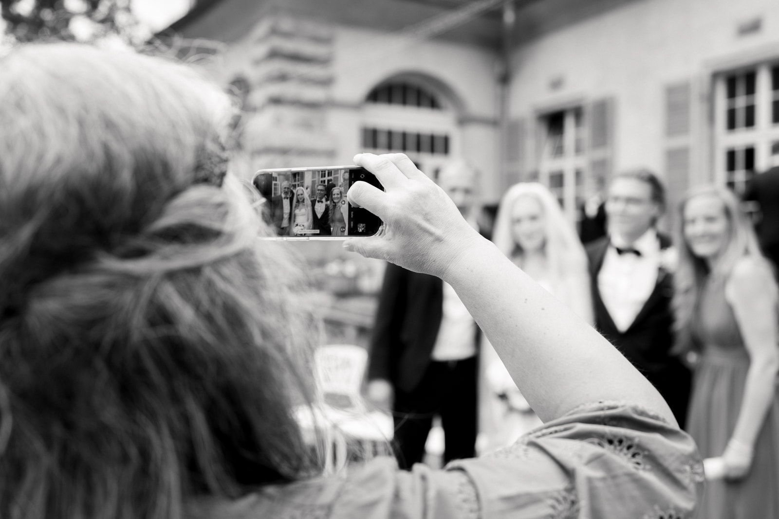 Hochzeitsgast fotografiert Brautpaar mit Smartphone bei Feier