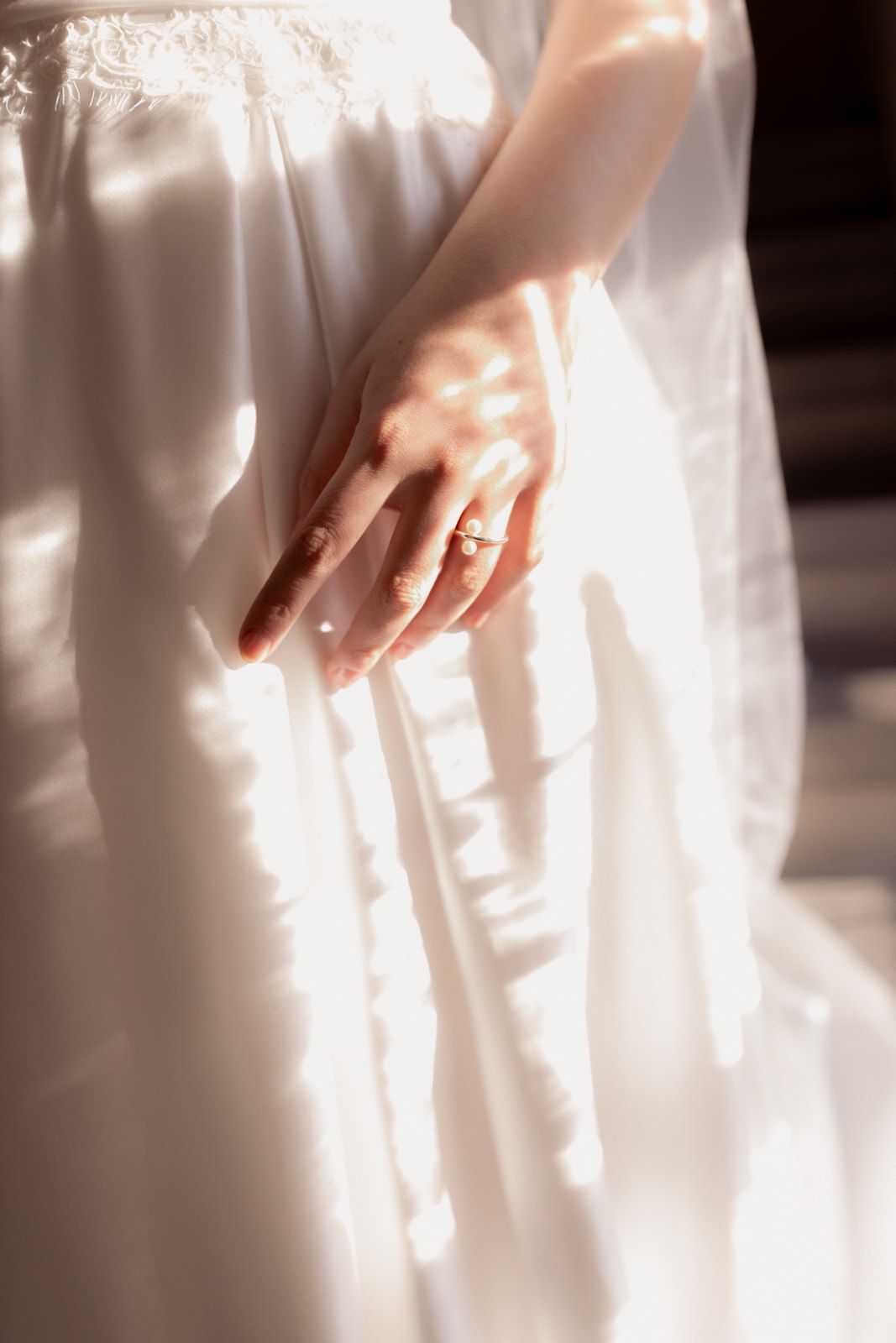 Bride's hand with wedding ring against white lace dress