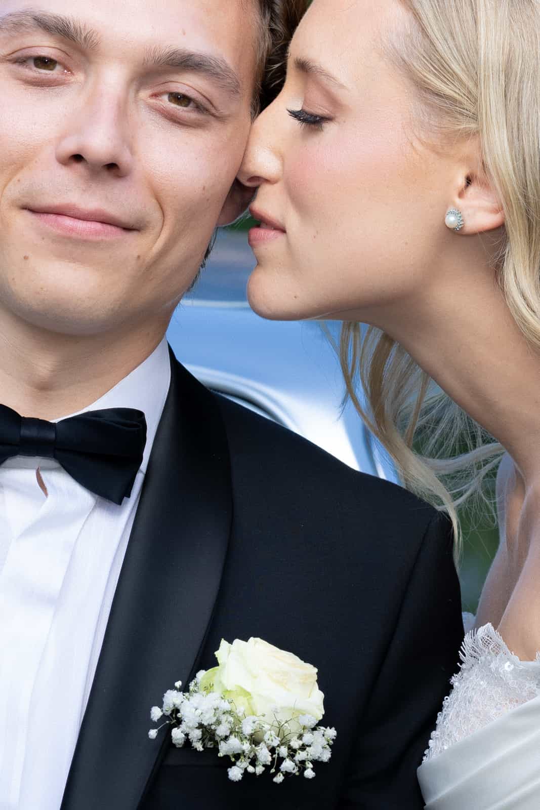 Bride kissing groom on cheek, close-up with rose boutonniere