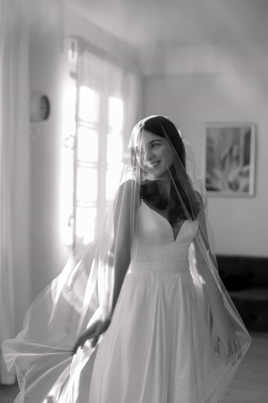 Smiling bride in white wedding dress with veil in natural window light