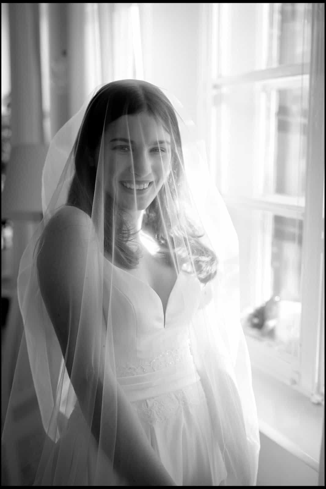 Smiling bride with veil in black and white photography in natural window light