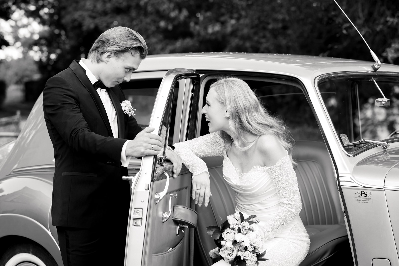 Groom opening car door and helping bride with bouquet out of vintage car