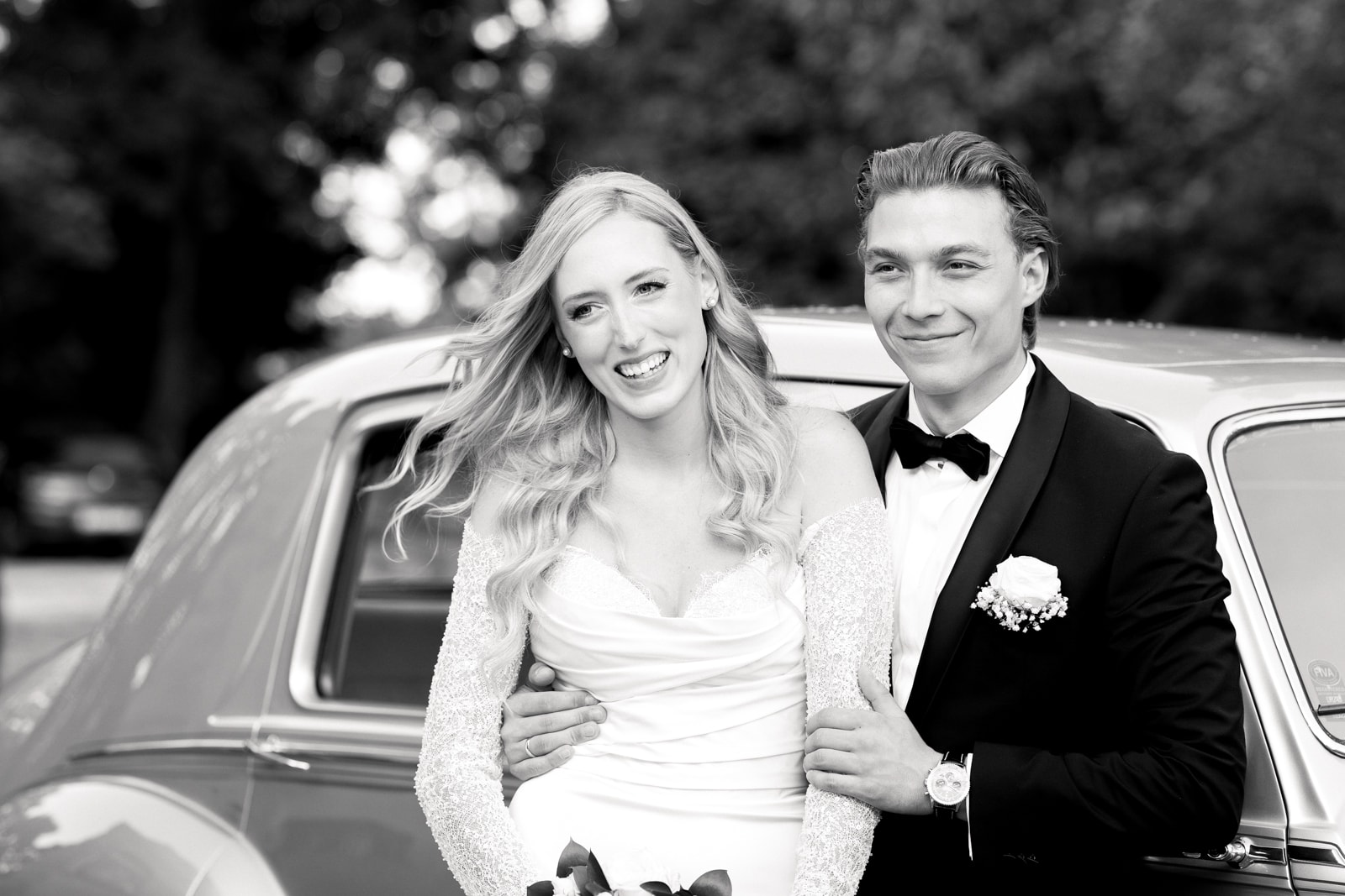 Happy bride and groom standing arm in arm in front of classic vintage car