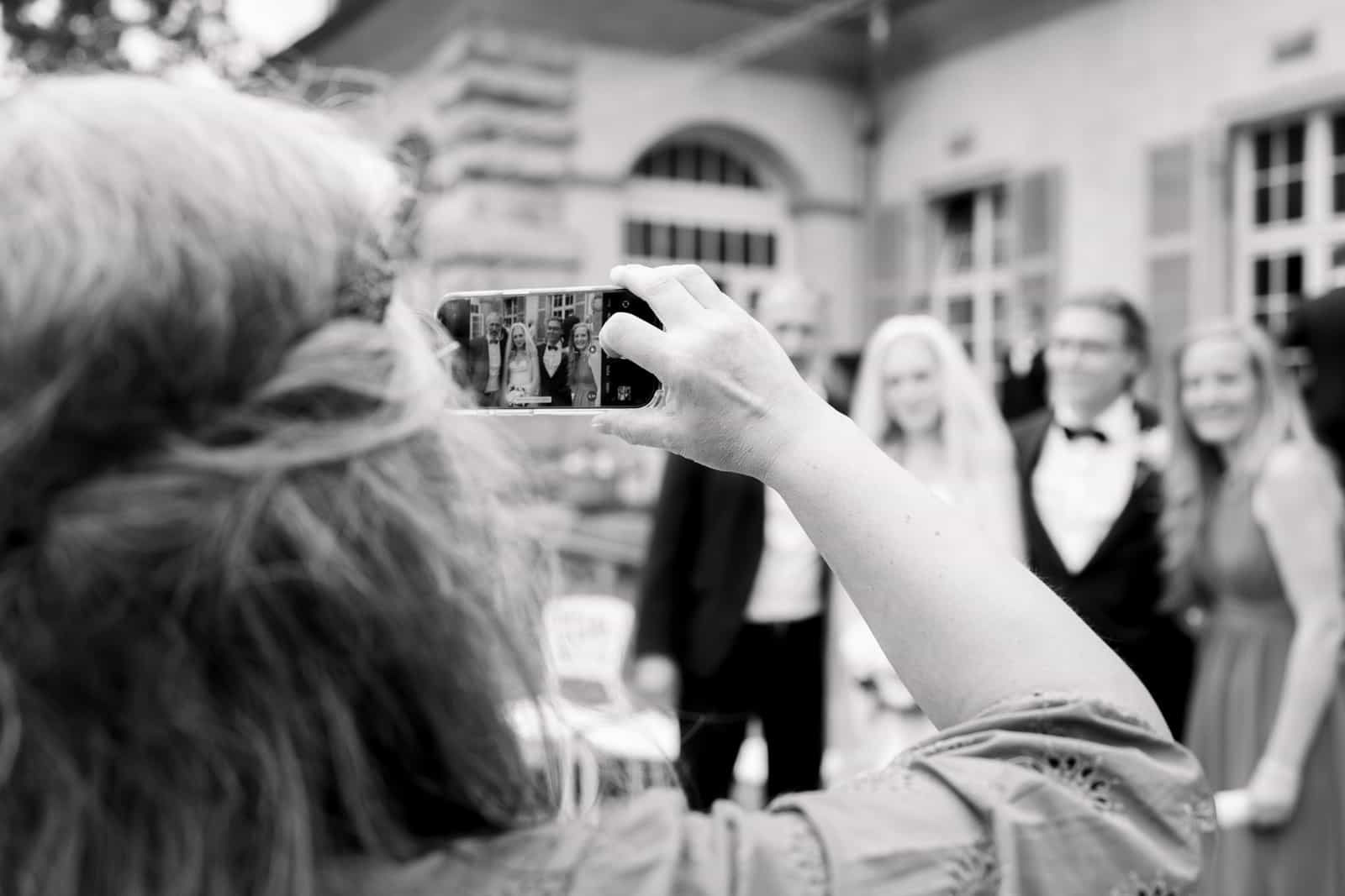 Wedding guest taking smartphone photo with couple blurred in background