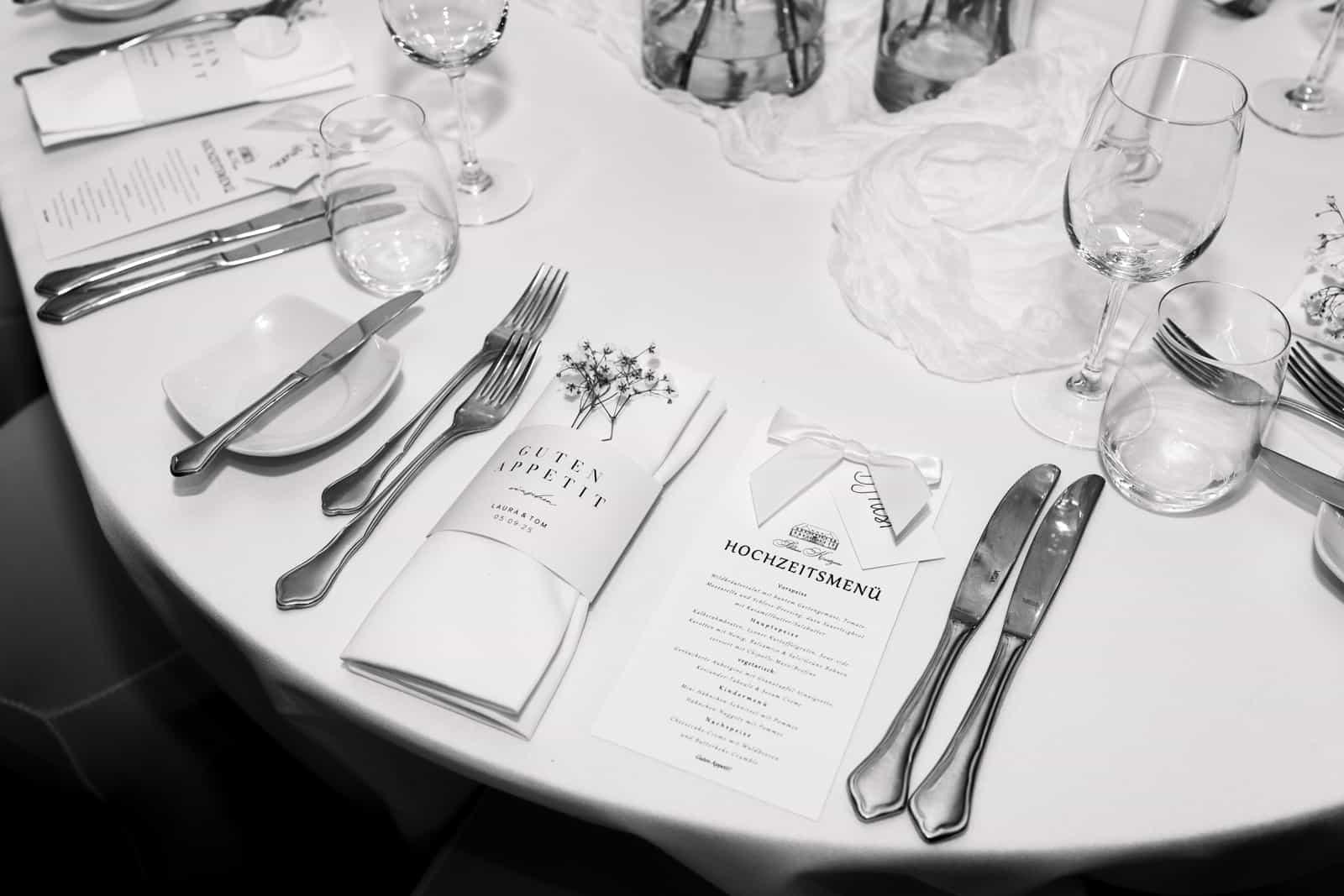 Black and white photo of elegantly set wedding reception table with menu cards, silverware and wine glasses